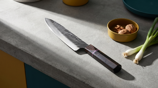 Haru forged 440C kitchen knives with dark ebony-style handles laid out on a raw concrete counter in hard morning light
